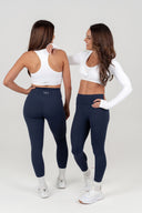 Two women wearing perform navy leggings and white tops, facing each showing scultping high waist flattering design