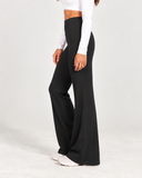 A woman shown from the side wearing a white long-sleeve crop top and black wide-leg pants against a plain light gray studio background.